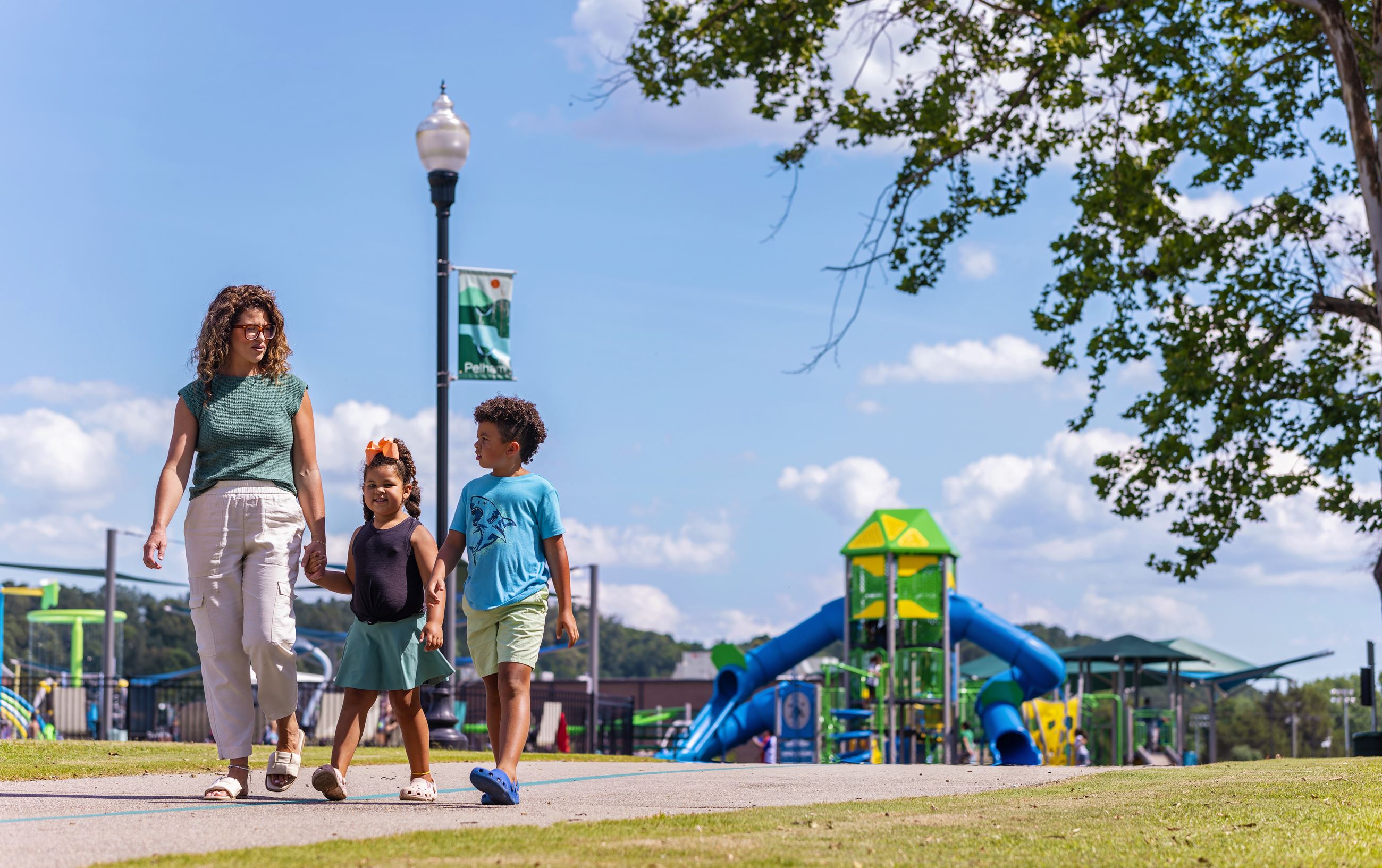 Mother and two young children walking on the trail with a playground in the background