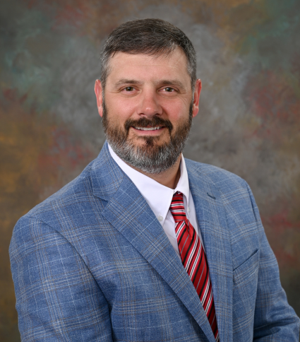 Councilmember Michael Harris wears a blue plaid jacket with gold highlights, and a red striped tie.